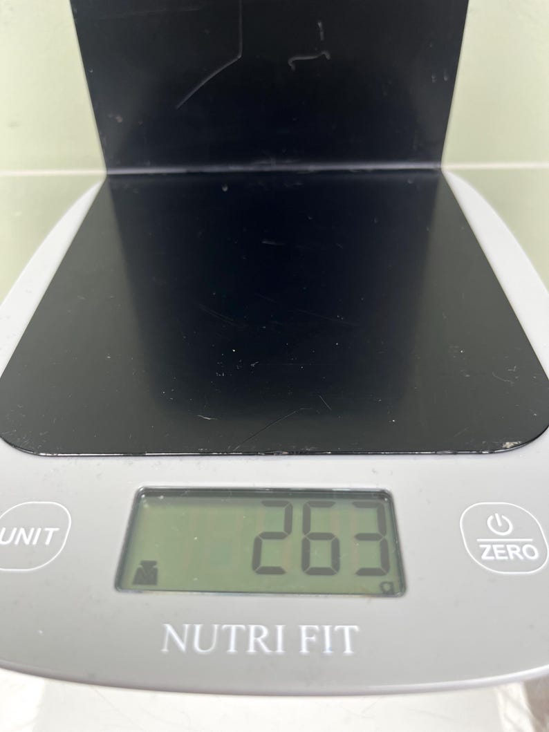 May include: A digital kitchen scale with a black surface and a grey base. The display shows the number 263. The scale has buttons labelled "UNIT" and "ZERO", and the brand name "NUTRI FIT" is visible.