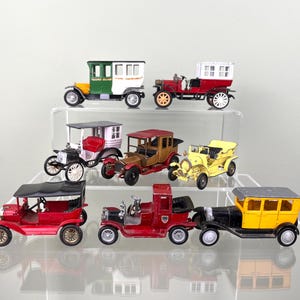 Può includere: Una collezione di sette auto giocattolo vintage, tutte di colori e stili diversi. Le auto sono disposte su un espositore a più livelli. Le auto sono tutte in buone condizioni e sembrano essere fatte di metallo.