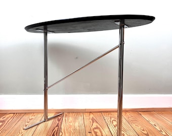 May include: A black oval-shaped table with a chrome base and a single support bar. The table is on a wooden floor.