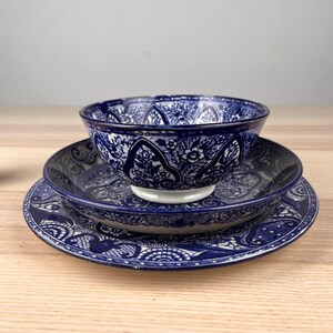 May include: A stack of three ceramic dishes featuring a deep blue and white floral pattern. The set includes a small bowl resting on a shallow bowl, which is placed on a larger dinner plate. Each piece displays intricate, repeating botanical motifs.