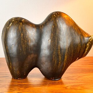 May include: A brown ceramic sculpture of an abstract animal with a smooth, glossy finish. The sculpture has a rounded, organic shape and is reminiscent of a stylized bear or bull.