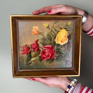 Könnte beinhalten: Gerahmtes Gemälde mit roten, gelben und orangen Rosen. Das Kunstwerk hat einen goldfarbenen Rahmen und zeigt einen Rosenstrauß mit grünen Blättern. Das Gemälde wird von zwei Händen gehalten.