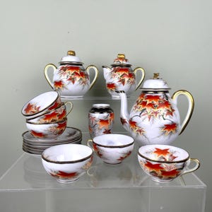 Könnte beinhalten: Ein Set aus drei Keramikbechern mit gesprenkelter, matter Oberfläche. Die Becher sind in Creme-, Hellgrau- und Dunkelgrautönen gehalten. Jeder Becher hat ein schlichtes, minimalistisches Design und einen abgerundeten Henkel.