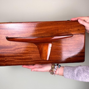 Könnte beinhalten: Ein an der Wand montiertes Holzmodell eines Segelboots mit Mahagoni-Finish. Das Modell ist auf einer rechteckigen Holzplatte montiert.