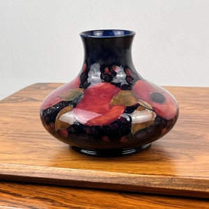 May include: A dark blue and red ceramic vase with a floral design. The vase has a wide base and a narrow neck.