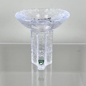 Peut inclure: Un bougeoir en verre transparent avec une base texturée en forme d'étoile et un large bol peu profond. Le bougeoir porte un logo Orrefors Sweden vert sur la base.