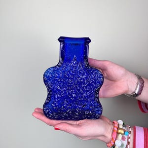 Könnte beinhalten: Eine kobaltblaue Glasvase mit einem strukturierten, geprägten Design. Die Vase hat einen breiten Boden und einen schmalen Hals.