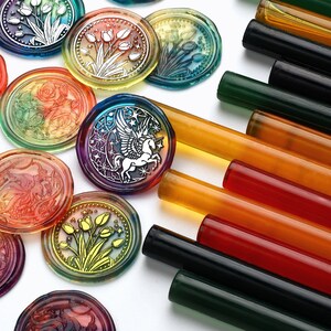 May include: Assortment of colourful wax seals with various designs, including a unicorn, flowers, and roses. The seals are arranged on a white surface with a variety of coloured wax sticks.