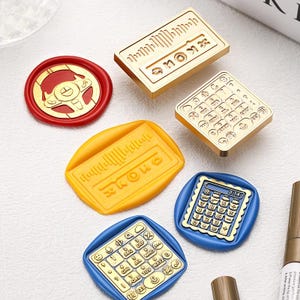 Op de afbeelding: Een verzameling decoratieve waszegels in verschillende vormen en kleuren. De zegels omvatten een rood stuurwiel, een gouden rekenmachine en een geel geluidsgolfontwerp. Andere zegels tonen een rekenmachine en een telefoontoetsenbord.
