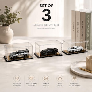 May include: A set of three rectangular clear acrylic display cases, each featuring a black base and a gold-colored platform. Inside each case is a miniature toy sports car: one silver, one black, and one white. The text reads SET OF 3 ACRYLIC DISPLAY CASE.