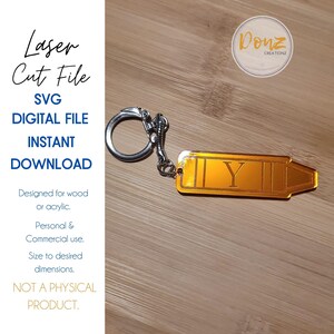 May include: Gold-colored metal keychain shaped like a crayon with the letter "Y" engraved on it. The keychain is attached to a silver metal ring.