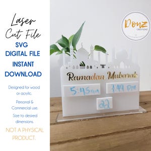 Peut inclure: Modèle de découpe laser blanc d'une mosquée avec une plante devant. Le motif comprend le texte "Ramadan Mubarak" et un espace pour écrire les heures et les dates.