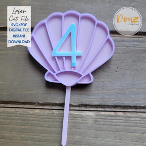 Puede incluir: Un adorno para pastel en forma de concha de color lavanda con el número 4 en azul claro en el centro. El adorno tiene un tallo largo para insertar en un pastel. El texto a la izquierda dice "Laser Cut File SVG/PDF DIGITAL FILE INSTANT DOWNLOAD."