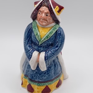 May include: A ceramic figurine of the Queen of Hearts from Alice in Wonderland. She is wearing a blue and yellow robe with a red and yellow crown. Her face is painted with a stern expression.
