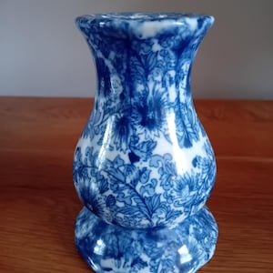 Puede incluir: Un jarrón de cerámica azul y blanco con un patrón floral. El jarrón tiene una base ancha y un cuello estrecho.
