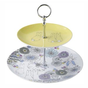 Puede incluir: Una bandeja de servir de dos niveles con asa plateada. El nivel superior es amarillo con ilustraciones de conejos. El nivel inferior presenta un estampado floral con conejos. Una pieza decorativa para servir postres o aperitivos.