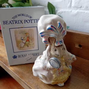 Peut inclure: Une figurine en porcelaine blanche représentant une souris portant un grand chapeau coloré et tenant une loupe. La figurine est de la collection Le Monde de Beatrix Potter et est fabriquée par Royal Albert.