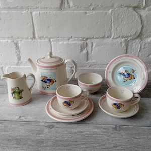 Puede incluir: Juego de té infantil color crema con ilustraciones de conejos. El juego incluye una tetera, una jarra de crema, dos tazas y platillos, un cuenco y un plato. Cada pieza tiene un borde rosa e ilustraciones de conejos.