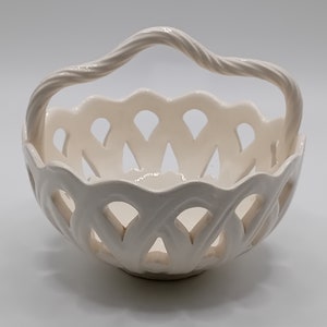 Könnte beinhalten: Weiße Keramikschale mit geflochtenem Design und einem gedrehten Griff. Die Schale ist perfekt für die Aufbewahrung von kleinen Gegenständen wie Obst oder Schmuck.