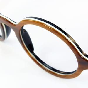 Könnte beinhalten: Nahaufnahme einer Brille mit braunem, schwarzem und weißem Rahmen. Die Brille hat eine runde Form mit einem dicken Rahmen. Die Bügel sind schwarz mit weißen Punkten. Die Gläser sind klar.