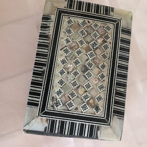 Peut inclure: Une boîte rectangulaire en bois avec un motif géométrique noir et blanc incrusté de nacre. La boîte a un couvercle à charnière et est décorée d'une bordure à rayures noires et blanches.