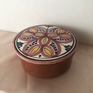 Peut inclure: Un récipient rond en céramique de couleur terre cuite avec un couvercle. Le couvercle présente un motif floral dans les tons de rose, jaune et bleu sur fond blanc. Le bord du couvercle est rose.