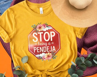 Może przedstawiać: Żółta koszulka z grafiką czerwonego znaku STOP, na którym widnieje napis "STOP being a PENDEJA" z kwiatowymi akcentami.