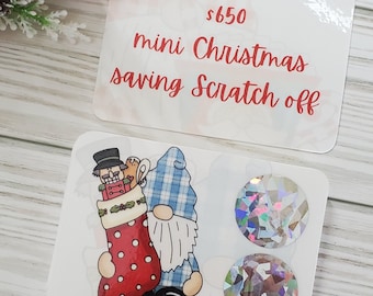May include: A mini Christmas saving scratch off card with a gnome and a stocking with a nutcracker inside. The card has two silver scratch off circles.