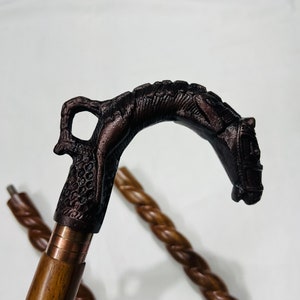 Pu&ograve; includere: Un bastone da passeggio in legno con un manico a forma di testa di cavallo dettagliato. Il manico &egrave; in metallo scuro e ha una fascia di colore rame attorno alla base. Il bastone &egrave; in legno e ha un design intrecciato.