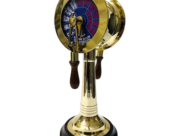 May include: A gold-colored ship's engine room telegraph with a blue face and red markings. The telegraph has two wooden handles and a black base.