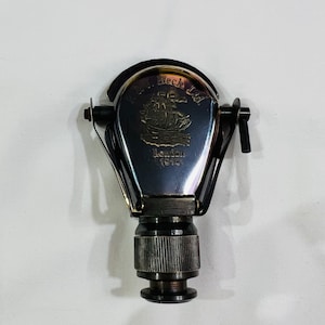 Puede incluir: Un tapón de botella de metal plateado con un grabado detallado de un barco y el texto "The Beck Ltd. London 1814".