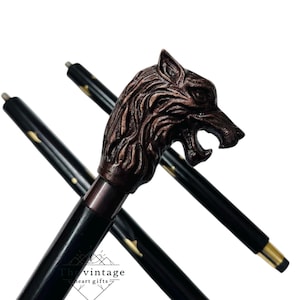 Puede incluir: Bastón negro con un mango de cabeza de lobo de bronce. El bastón tiene detalles dorados y el texto "The vintage heart gifts" es visible. La cabeza de lobo está detallada con la boca abierta.