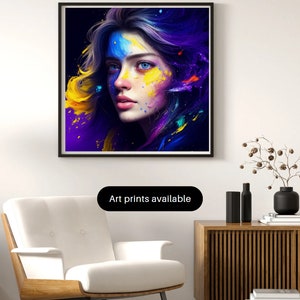 Puede incluir: Impresión artística enmarcada que presenta un retrato de una persona con ojos azules y salpicaduras de pintura coloridas en la cara y el cabello. La obra de arte se exhibe en una pared blanca sobre un sillón blanco y un mueble de madera. El texto en la imagen dice "Art prints available."