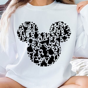 Puede incluir: Sudadera blanca con una silueta negra de la cabeza de Mickey Mouse formada por varios personajes de Disney.