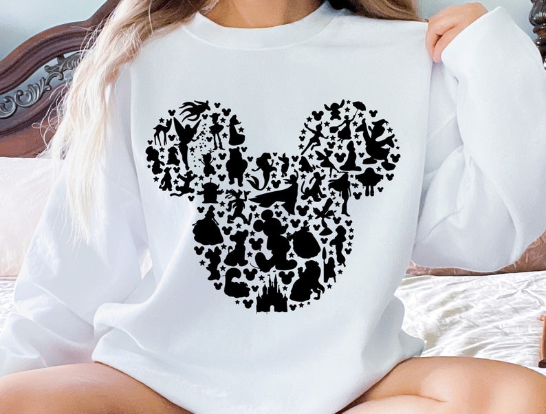 Puede incluir: Sudadera blanca con una silueta negra de la cabeza de Mickey Mouse formada por varios personajes de Disney.