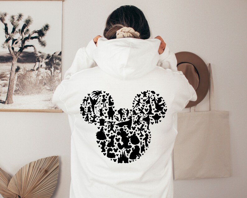 Puede incluir: Sudadera blanca con una silueta negra de la cabeza de Mickey Mouse formada por varios personajes de Disney.