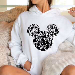 Puede incluir: Sudadera con capucha blanca con una silueta negra de Mickey Mouse formada por varios personajes de Disney.