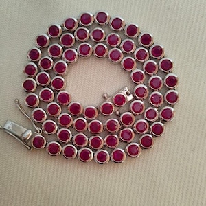 Puede incluir: Un collar de cadena de plata con piedras redondas de rubí rojo.