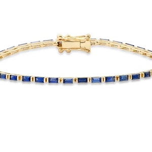 May include: A gold bracelet with a row of blue baguette-shaped sapphires.