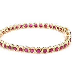 Pode incluir: Uma pulseira de ouro com uma fileira de pedras redondas de rubi vermelho.