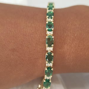 May include: A gold bracelet featuring a line of oval green gemstones and smaller clear stones.