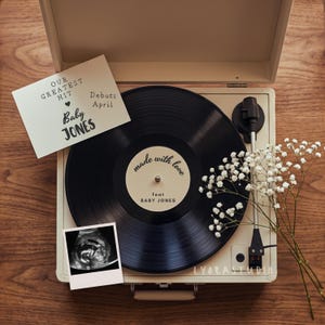 May include: A vintage record player with a black vinyl record that reads "made with love feat BABY JONES." A card says "OUR GREATEST HIT Baby JONES Debuts April." An ultrasound photo is also present.