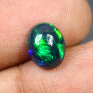 Puede incluir: Una piedra preciosa de ópalo ovalada de color verde oscuro y negro con destellos iridiscentes.