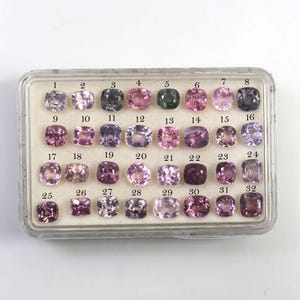 Puede incluir: Una colección de 32 piedras preciosas en una caja de plástico transparente. Las piedras son de varios tonos de rosa, morado, verde y gris. Cada gema está numerada del 1 al 32.