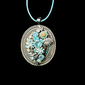 May include: A silver pendant necklace featuring a round blue and white floral design. The pendant is encircled by a silver frame with a textured pattern.