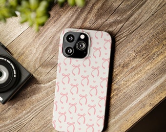 May include: A white phone case with a pink bow pattern. The case has a camera lens cutout and a white background.