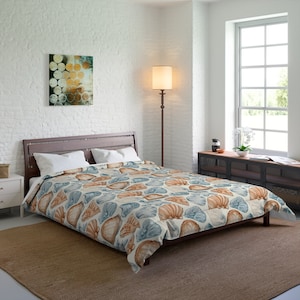 May include: A white duvet cover with a seashell pattern in shades of blue and orange. The duvet cover is on a bed with a wooden headboard and white pillows. The bed is in a bedroom with a white brick wall, a floor lamp, and a window.