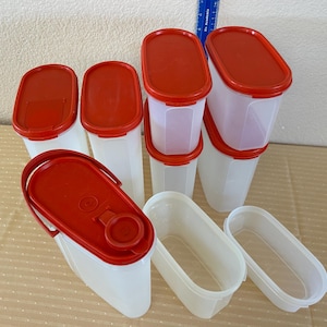 May include: A collection of white plastic food storage containers with red lids. The containers are various sizes and shapes, including oval and rectangular. Some have hinged lids, and others have separate lids.
