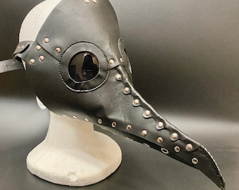 May include: A black leather plague doctor mask with a long beak and silver studs. The mask has a clear plastic eye piece.