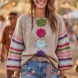 Op de afbeelding: Een beige gehaakte trui met kleurrijke gestreepte mouwen en bloemenapplicaties. De trui wordt gecombineerd met denim shorts met bloemenborduurwerk. Een riem met patroon en armbanden maken de bohemian look compleet.